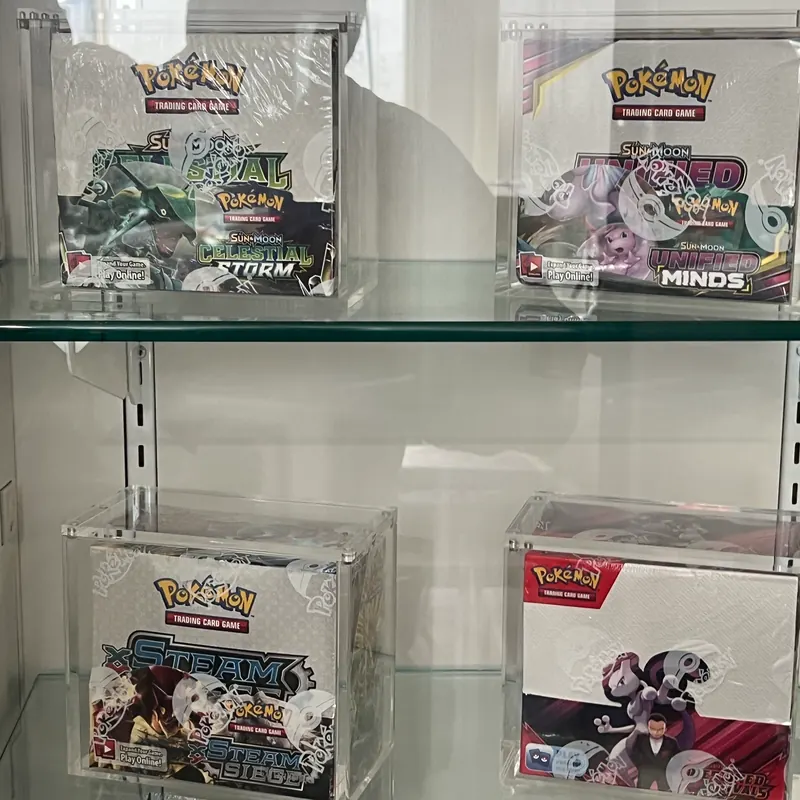 Vintage Pokémon booster boxes — Celestial Storm, Unified Minds, Steam Siege — sealed in acrylic cases in the Showcase